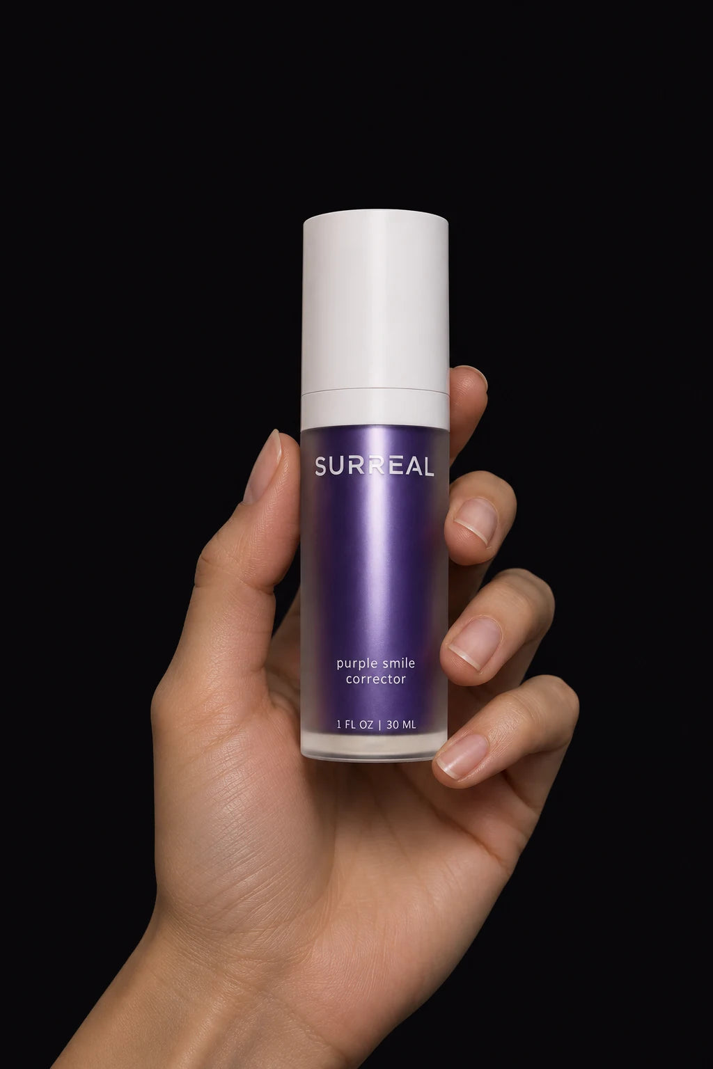 A hand holding the purple SURREAL Smile Corrector bottle with its white cap